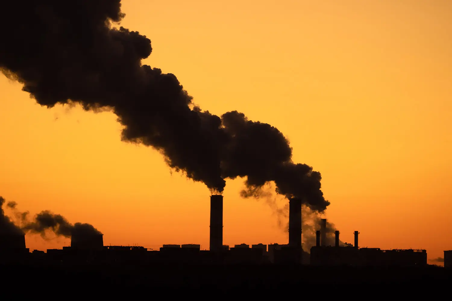 Silhouettes of the dark smoke clouds from tall chimneys of the industrial plant